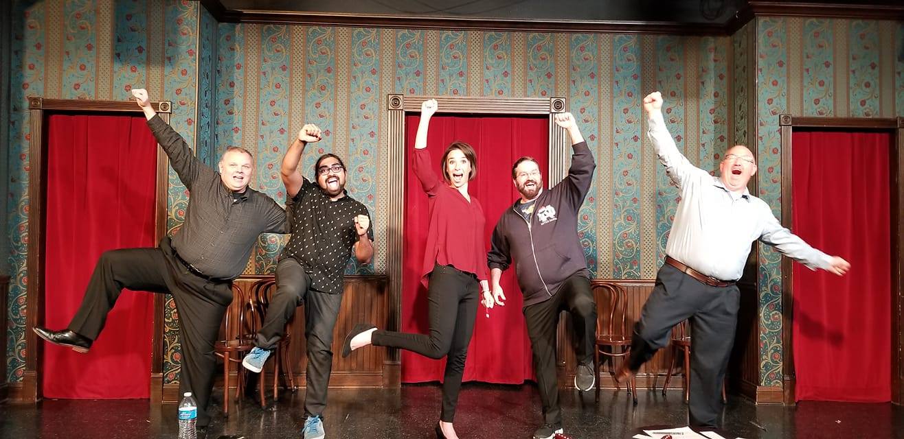 Five improv performers each lifting one fist high on stage